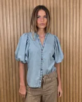 Camisa de algodón a rayas color beige y blanco, con escote en V, cuello mao y mangas cortas abullonadas. Cuenta con cierre frontal de botones oscuros.