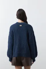 Sweater de punto color marrón chocolate, con cuello redondo, mangas largas abullonadas y puños ajustados. Presenta un diseño de textura acanalada horizontal y silueta relajada.