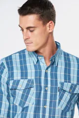Camisa de manga larga confeccionada en viyela, con diseño de cuadros en tonos azules y blancos. Presenta cuello clásico, cierre frontal con botones y dos bolsillos delanteros con solapa y botón.