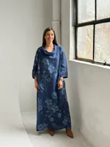 Vestido largo de lino azul marino con estampado floral en tonos más claros, de corte amplio, con cuello tipo cowl y mangas largas.