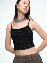 Top de tirantes finos color negro con estampado de pequeñas flores blancas, confeccionado en tejido acanalado con terminación de ruedo ondulado.