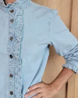 Camisa de denim con volados verticales a lo largo de la botonadura frontal y cuello alto. Presenta mangas largas con puños elásticos y detalle de volados en los mismos.