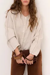 Chaqueta de lino color beige, de manga larga, con cuello redondo y cierre frontal de botones a presión con solapa.