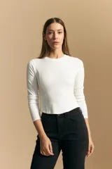 Remera blanca de manga larga con tejido acanalado, cuello redondo y corte ajustado al cuerpo. Presenta costuras verticales que definen la silueta.