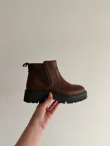 Bota corta de cuero color marrón con suela track dentada y cierre lateral.