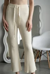 Pantalón de lanilla color crudo, de corte acampanado y tiro alto. Presenta una textura acanalada, cintura elástica con cordón ajustable y terminaciones con borde ondulado en el ruedo.