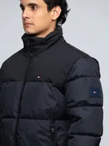 Campera puffer Tommy Hilfiger de color negro, con diseño acolchado, cuello alto y cierre frontal de cremallera. Cuenta con bolsillos laterales con cierre, el logo de la marca bordado en el pecho y un parche con el logo en la manga.