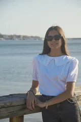 Blusa blanca de algodón con cuello bobo grande con volados, mangas cortas abullonadas con puños elásticos y cierre posterior con botones.
