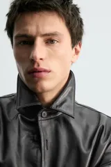 Sobrecamisa de corte regular confeccionada en piel napa negra, con cuello solapa, cierre frontal de botones y mangas largas con puños abotonados.