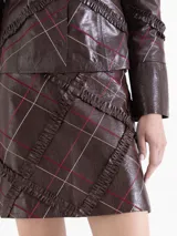 Minifalda de cuero vacuno con acabado brillante, diseño de cuadros bordados y volados de cuero que aportan textura.