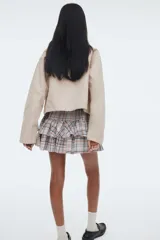 Pollera mini a cuadros en tonos tierra, azul marino y blanco. Diseño de tiro alto con elástico revestido en la cintura y cordón ajustable. Presenta dos volados horizontales que le dan volumen.