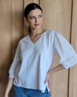 Remera blanca con cuello en V, cuerpo de algodón y mangas abullonadas de encaje bordado con puños elásticos.