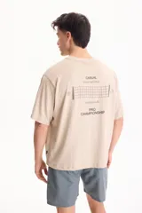 Remera beige de manga corta y corte oversize, con estampa en la espalda con temática de tenis y texto descriptivo.