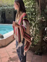 Chal tejido a mano en lana merino, con diseño de jacquard geométrico multicolor a rayas en tonos crudo, fucsia, verde, amarillo y marrón, terminado con flecos en los extremos.