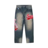 Pantalón de jean Supreme en colaboración con Mitchell & Ness, de corte holgado y lavado desgastado. Presenta parches bordados con el logo de Supreme y el diseño de los Atlanta Braves en las piernas, además del logo de la MLB en el bolsillo delantero.