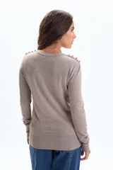 Buzo de punto color beige, con cuello redondo, manga larga y botones decorativos en los hombros y puños.