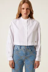 Camisa blanca corta de corte recto con cuello mao, mangas anchas con puños ajustados y aberturas trenzadas en las mangas. Incluye medalla de bronce con logo "TRS".