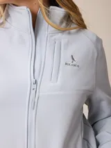 Campera softshell blanca con cierre frontal completo, cuello alto y bolsillos laterales. Presenta un bolsillo vertical con cierre en el pecho y el logo de la marca bordado.