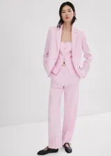 Blazer de lino color rosado, de diseño recto con cuello en pico y solapas con muesca. Cuenta con manga larga, dos bolsillos de ribete delanteros y cierre frontal de un botón.