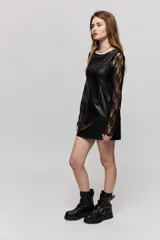 Vestido corto de símil cuero negro, de corte recto, escote amplio y sin mangas, combinado con mangas largas de encaje negro.