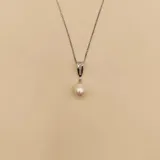 Collar de cadena fina de plata 925 con un dije que presenta una perla de río blanca y una pieza superior decorada con circonias engastadas.