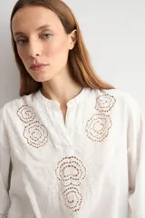 Blusa blanca de corte holgado con cuello mao y escote en V. Presenta detalles de bordado calado en el pecho y en los puños de las mangas tres cuartos.