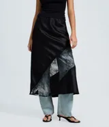 Pollera midi de satén negro con corte evasé, cintura elástica y detalle de entremedio de encaje aplicado en diagonal.