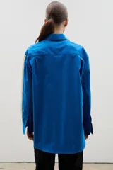 Camisa de corte holgado y largo medio, color negro con detalle de franja lateral en color crema a lo largo de las mangas. Presenta cuello clásico, cierre frontal con botones y tajos laterales en el ruedo.