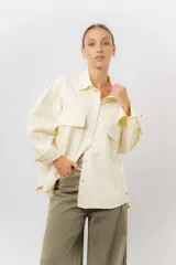 Sobrecamisa de gabardina liviana color crema, con corte oversize, cuello clásico, cierre frontal con botones a presión y dos bolsillos delanteros con solapa.