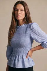 Blusa negra de algodón peinado, con cuerpo fruncido tipo smock, cuello redondo con volados y mangas largas abullonadas.