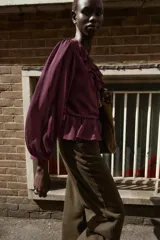 Blusa de color bordó con escote en V profundo adornado con volantes, mangas largas con puños y detalle de peplum en el ruedo. Cuenta con cierre frontal de botones forrados en la misma tela.