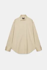 Camisa oversize color beige con mezcla de algodón, cuello smoking, manga larga con puños anchos y cierre frontal con botones ocultos por solapa.