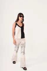 Pantalón de lino color crema, corte flared y tiro medio alto. Presenta cierre y trabilla metálica, bordado en la pretina, diseño de palmera egipcia estampada por serigrafía en la pierna y pespuntes a contratono en el bajo.