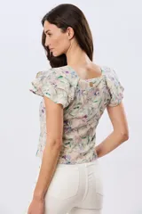 Camisa de lino estampada con diseño floral en tonos lila y verde, mangas cortas con volados y cierre frontal con botones.