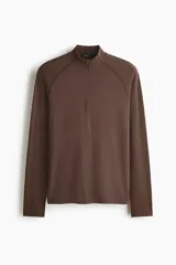 Remera deportiva marrón con cuello alto, cierre frontal parcial y mangas largas raglán, confeccionada en tejido técnico con paneles texturizados y corte ajustado.
