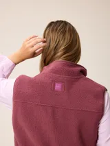 Chaleco de sherpa color beige con cierre frontal completo, cuello alto y bolsillo con cierre en el pecho que incluye un detalle circular con logo.