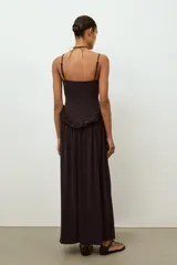 Vestido largo de color negro con escote recto y tirantes finos ajustables. Presenta un diseño con detalle de volante tipo peplum en la cintura y falda con caída fluida.
