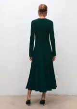 Vestido midi de corte evasé en color verde oscuro, con cuello redondo y mangas largas. Presenta un diseño con detalle de godets en la falda y cierre de cremallera en la parte posterior.