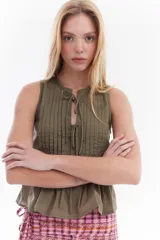 Blusa blanca sin mangas de algodón, con diseño de tablas frontales y escote con lazos para atar.