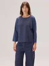 Camisa de manga larga con cuello redondo, confeccionada en una mezcla de algodón y tencel. Presenta un diseño de paneles con costuras a la vista en color contrastante y corte recto.