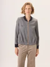 Chaqueta tipo bomber de lana con estampado de espiga en tonos grises. Presenta cuello, puños y ruedo en tejido elástico negro, cierre frontal dorado y bordado sutil en el pecho.