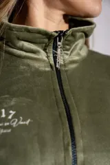 Buzo de plush color verde oliva, con cuello alto y cierre frontal parcial. Presenta mangas largas con puños elásticos y un pequeño bordado en el pecho.