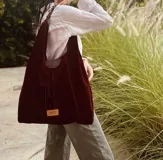 Cartera tipo hobo de gamuza color borgoña con flecos y asa corta de cuero marrón.