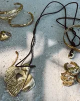 Collar con dije grande de bronce con forma orgánica y textura rugosa, suspendido de un cordón negro. Incluye cordones intercambiables.