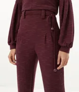 Pantalón jogger color borgoña confeccionado en malla flamê texturizada, con cintura con trabillas largos, cordón para amarre, pliegues delanteros y barra ajustada con pliegues.