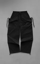 Pantalón oversize estilo cargo negro, confeccionado en tejido técnico liviano. Cuenta con cintura elástica con cordón ajustable, bolsillos laterales envolventes de gran tamaño con cordones y tancas de ajuste, y elásticos regulables en los tobillos.