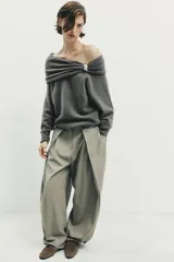 Jersey de punto color gris oscuro, con escote recto tipo off-shoulder, manga larga y detalle de aplique metálico en el hombro. Presenta acabados en rib en puños y ruedo.