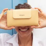 Billetera larga color beige, con textura granulada, solapa frontal con cierre magnético y logo de la marca grabado. Incluye correa de mano extraíble y compartimento principal con cierre.