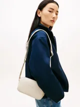 Cartera tipo bandolera de diseño compacto y líneas redondeadas, marca Tommy Hilfiger. Está confeccionada en poliuretano con acabado liso de color beige, cierre de cremallera y cuenta con una inscripción de la marca en bajo relieve en la parte delantera. Incluye una correa cruzada ajustable de jacquard tonal con el logo de la marca.