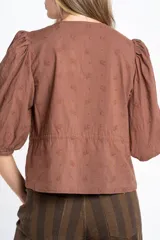 Blusa negra de algodón con diseño de broderie, mangas tres cuartos abullonadas, cierre frontal con botones y detalle de cordón ajustable en la cintura.